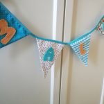 Guirlande de fanions en tissus (bleu turquoise, orange, gris et rouge) et personnalisable avec prénom