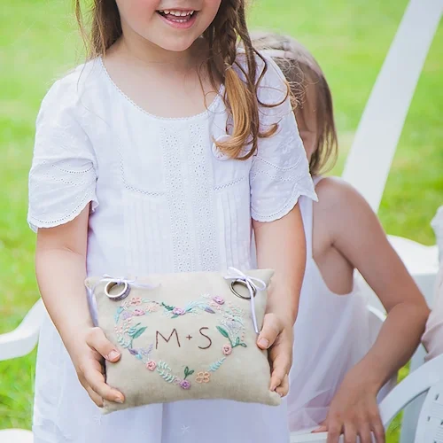 Carrousel_CreationsMains_06 Coussin d’alliances personnalisé brodé avec initiales, porté par une enfant lors d’un mariage.